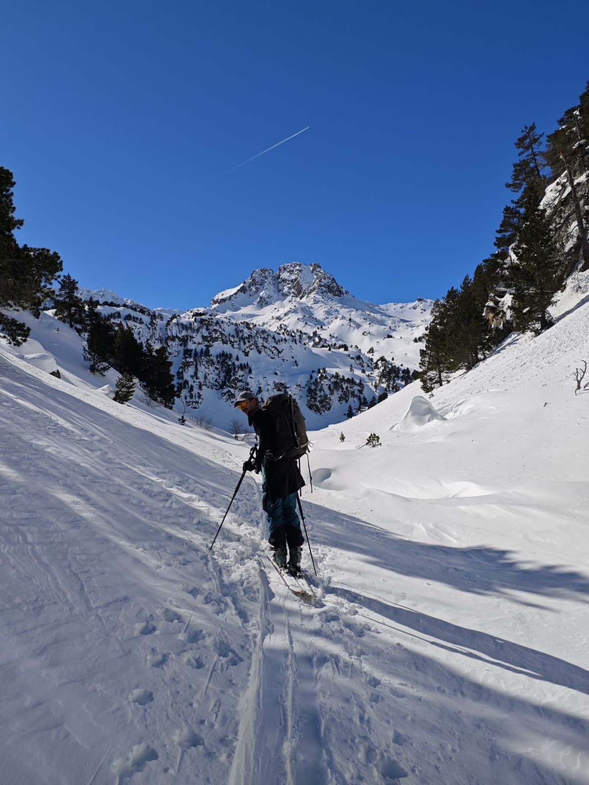 Esquiador de travesía subiendo hacia el pico con cielo azul